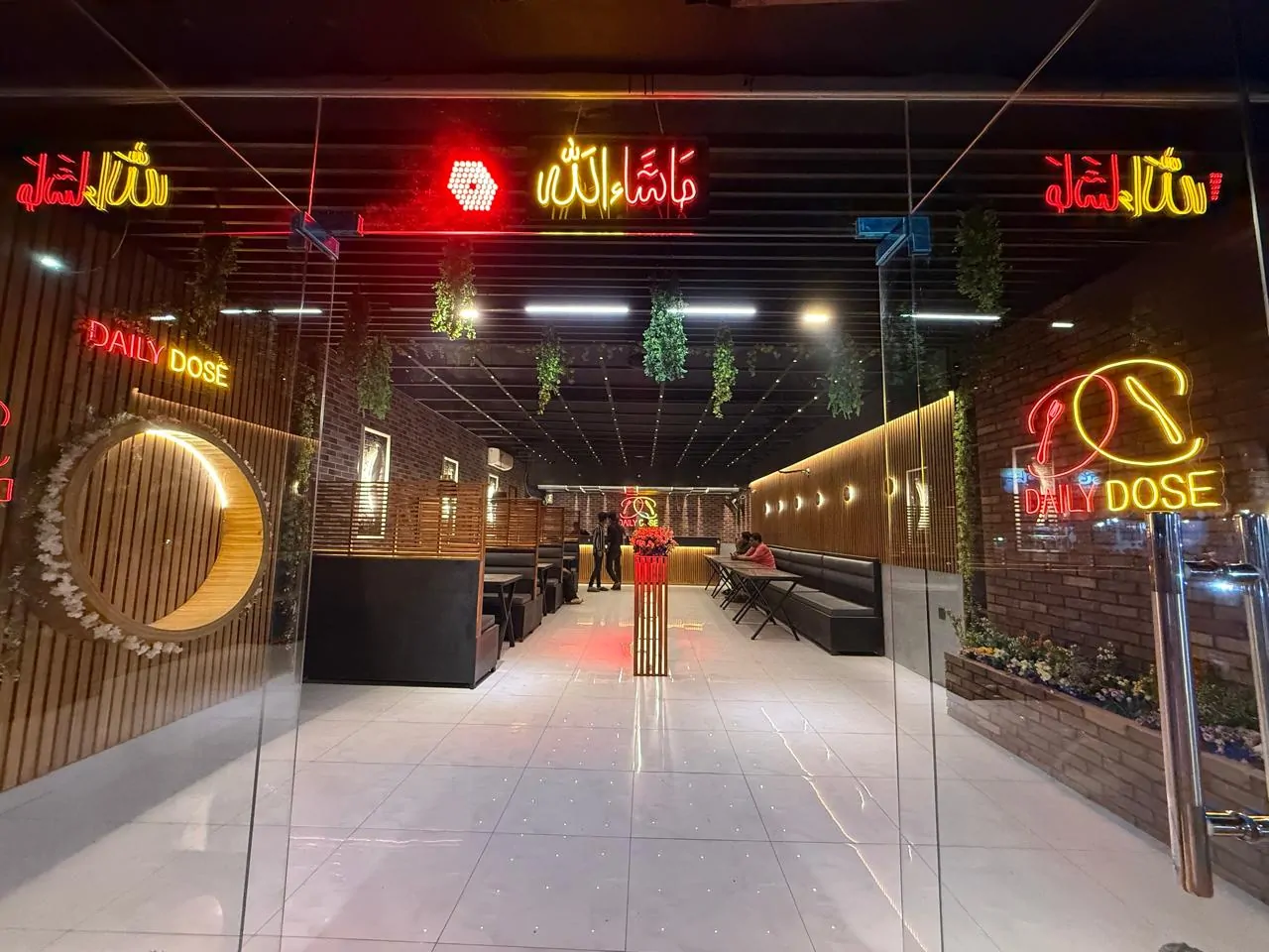 Cafe entrance through glass doors, with neon signage, hanging greenery and booths