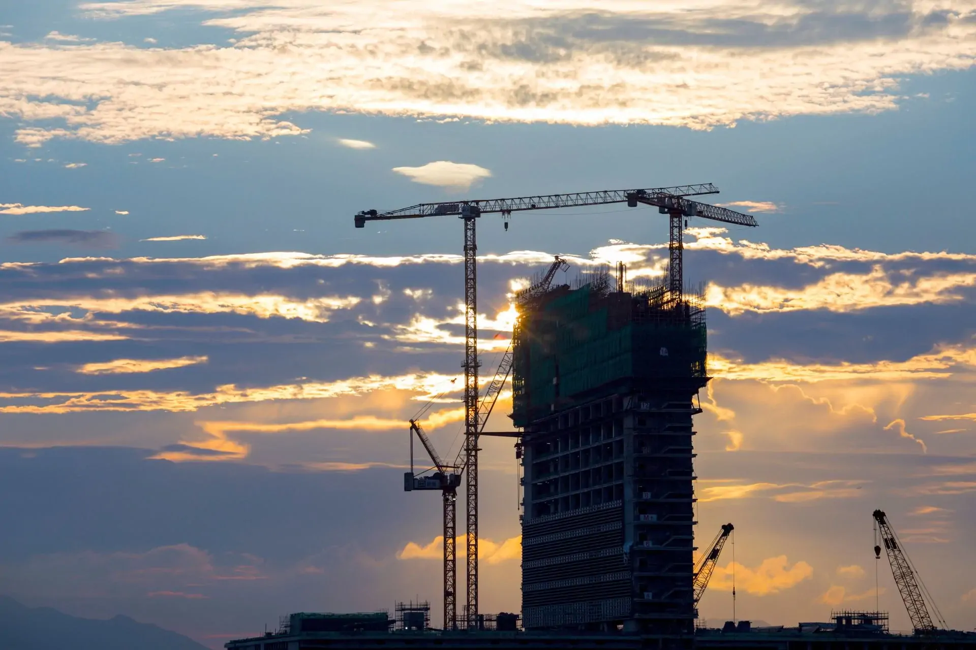 Building under construction with tower cranes at sunset