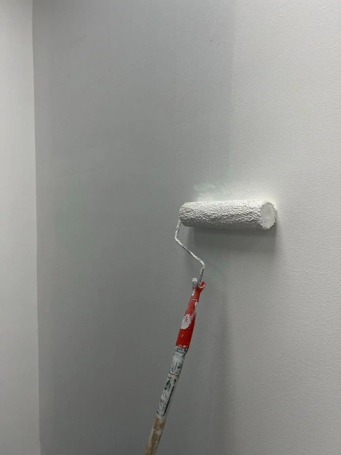 Paint roller applying white paint to a wall